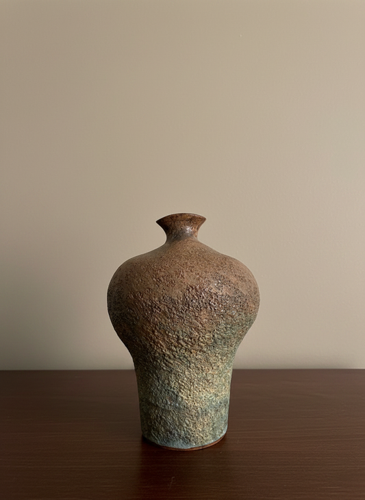 earthy coloured textured vase on a brown table against a wall