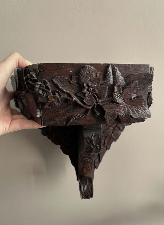 carved wooden wall bracket being held against a wall with a hand in the shot