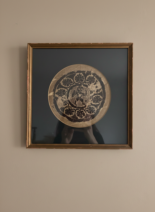 A framed coptic textile roundel feauturing a warrier surrounded by leaves against a taupe coloured wall