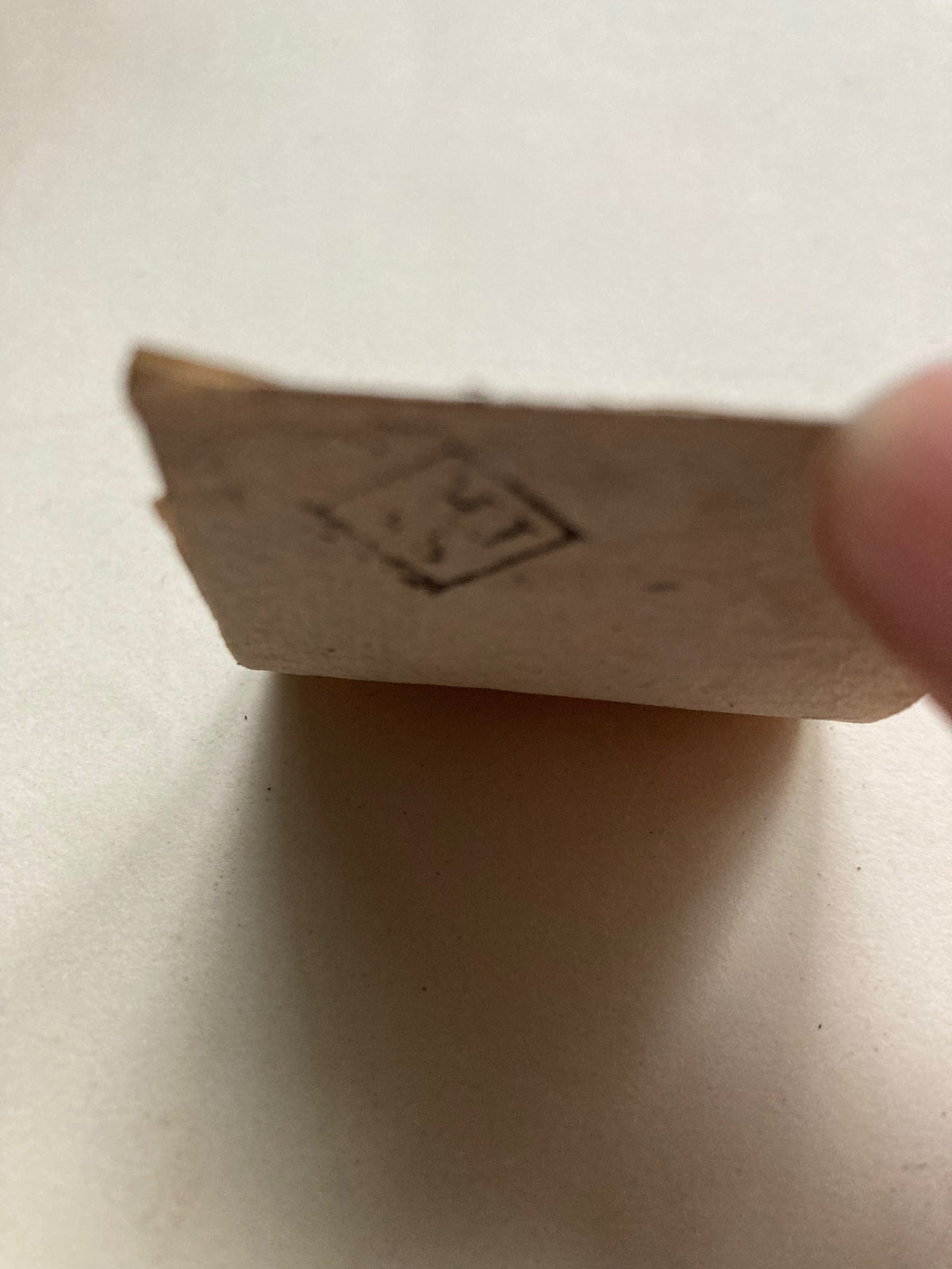 reverse of an etching with a symbol on it to mark the piece was part of the inventory of sir joshua reynolds, held by a finger against a light background