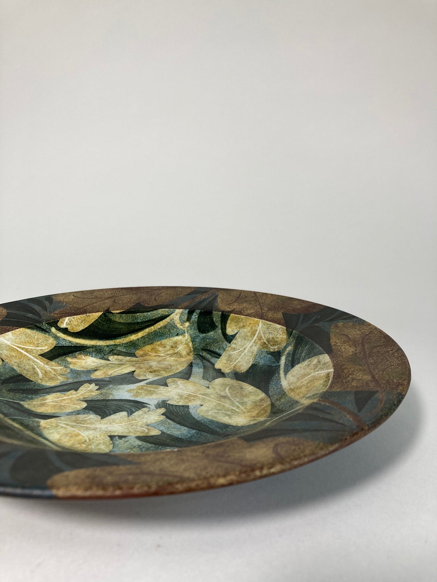 A highly decorative plate by Ralph Jandrell with a green and brown pattern and mixed glaze side view
